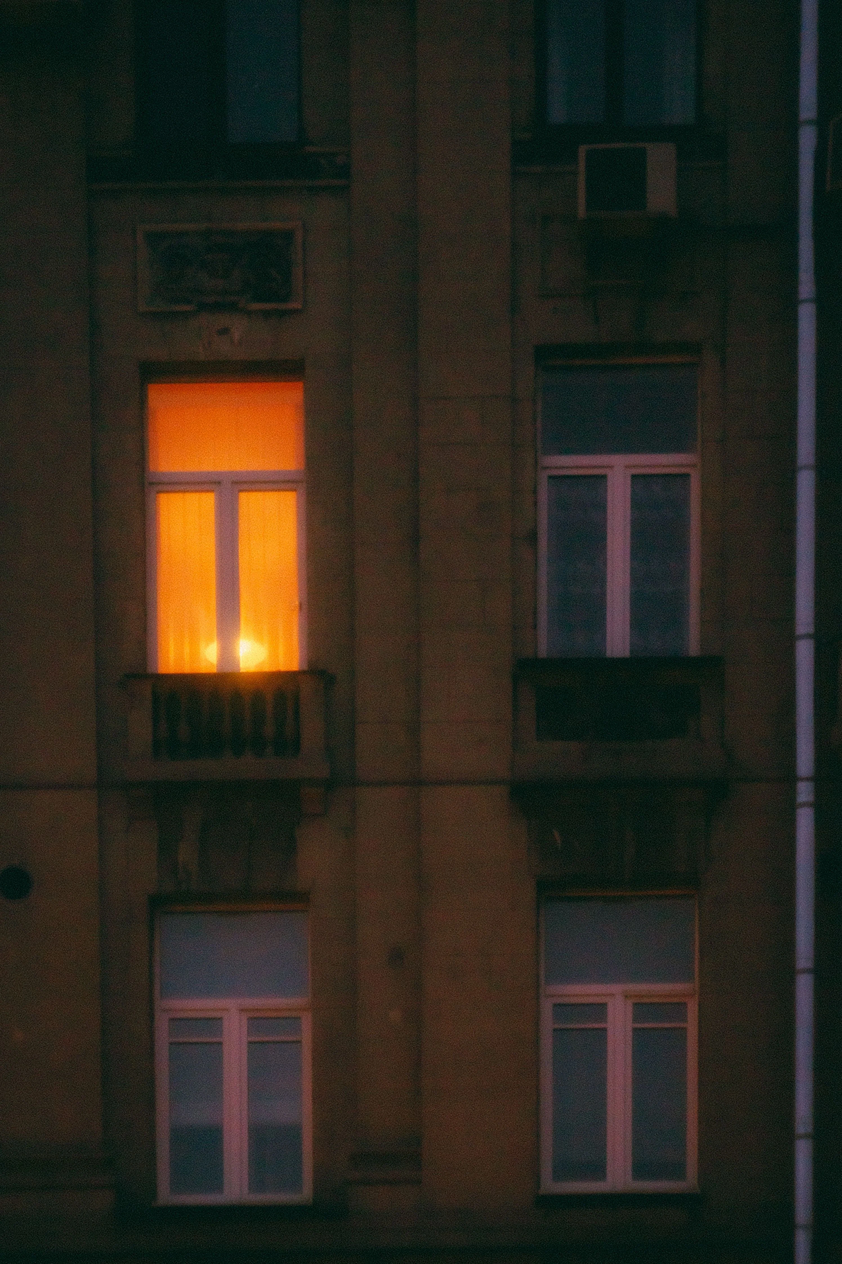 A single warmly lit window on a dark building at night.
