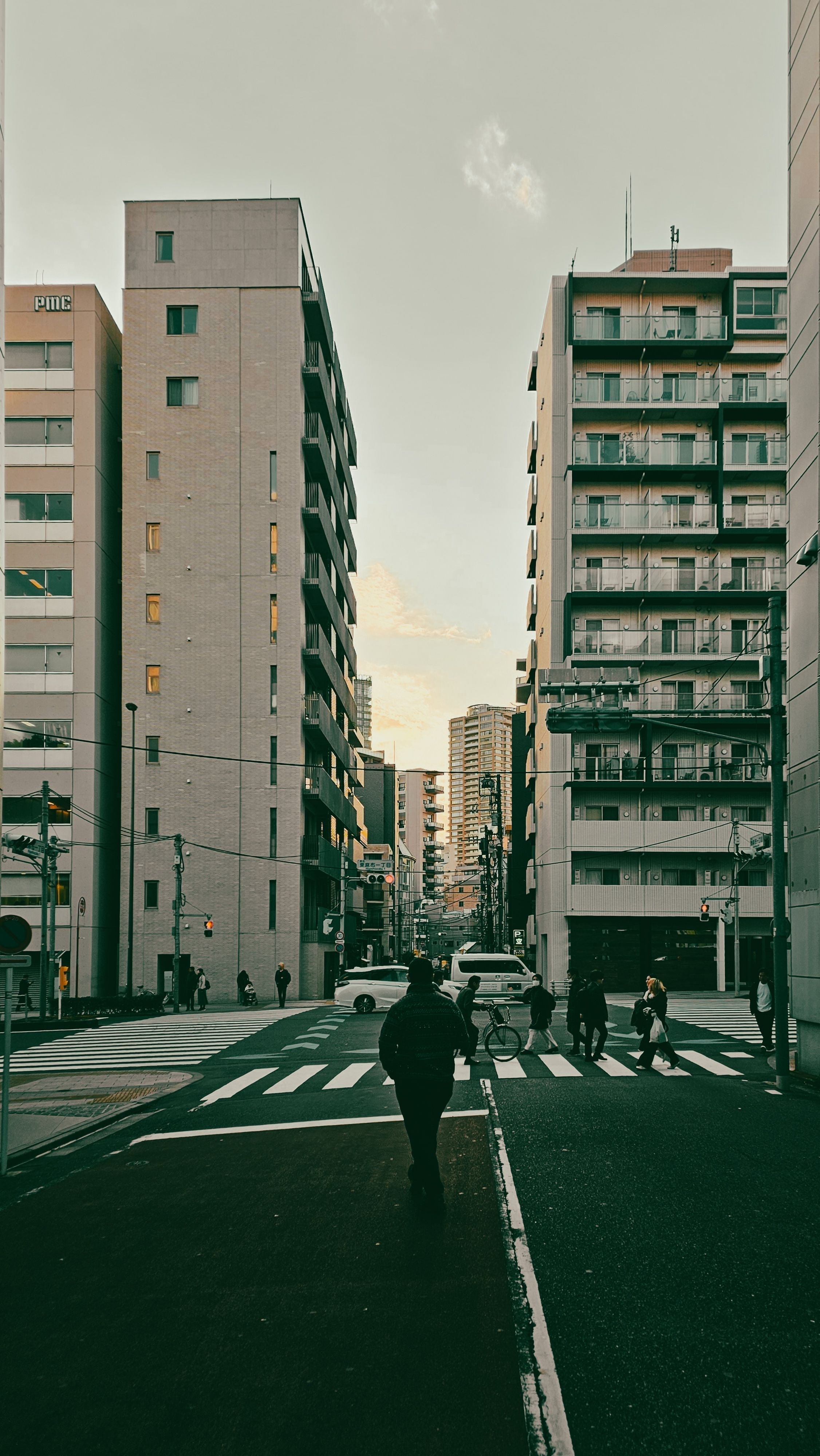 A person walks across a quiet city intersection between tall apartment buildings at sunset.