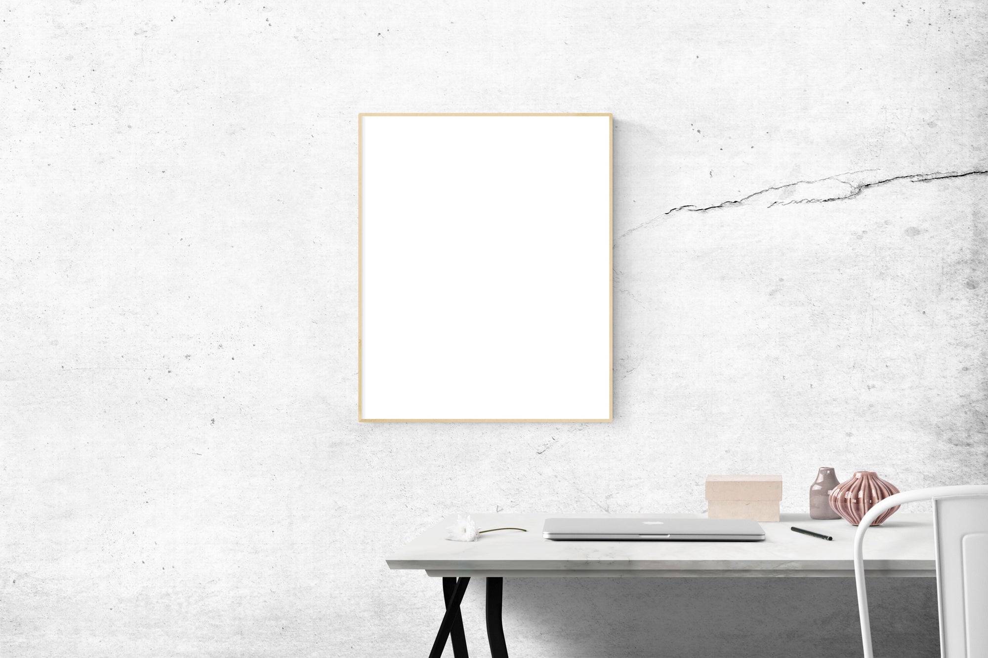 A minimalist workspace with a laptop, blank frame, and textured white wall.