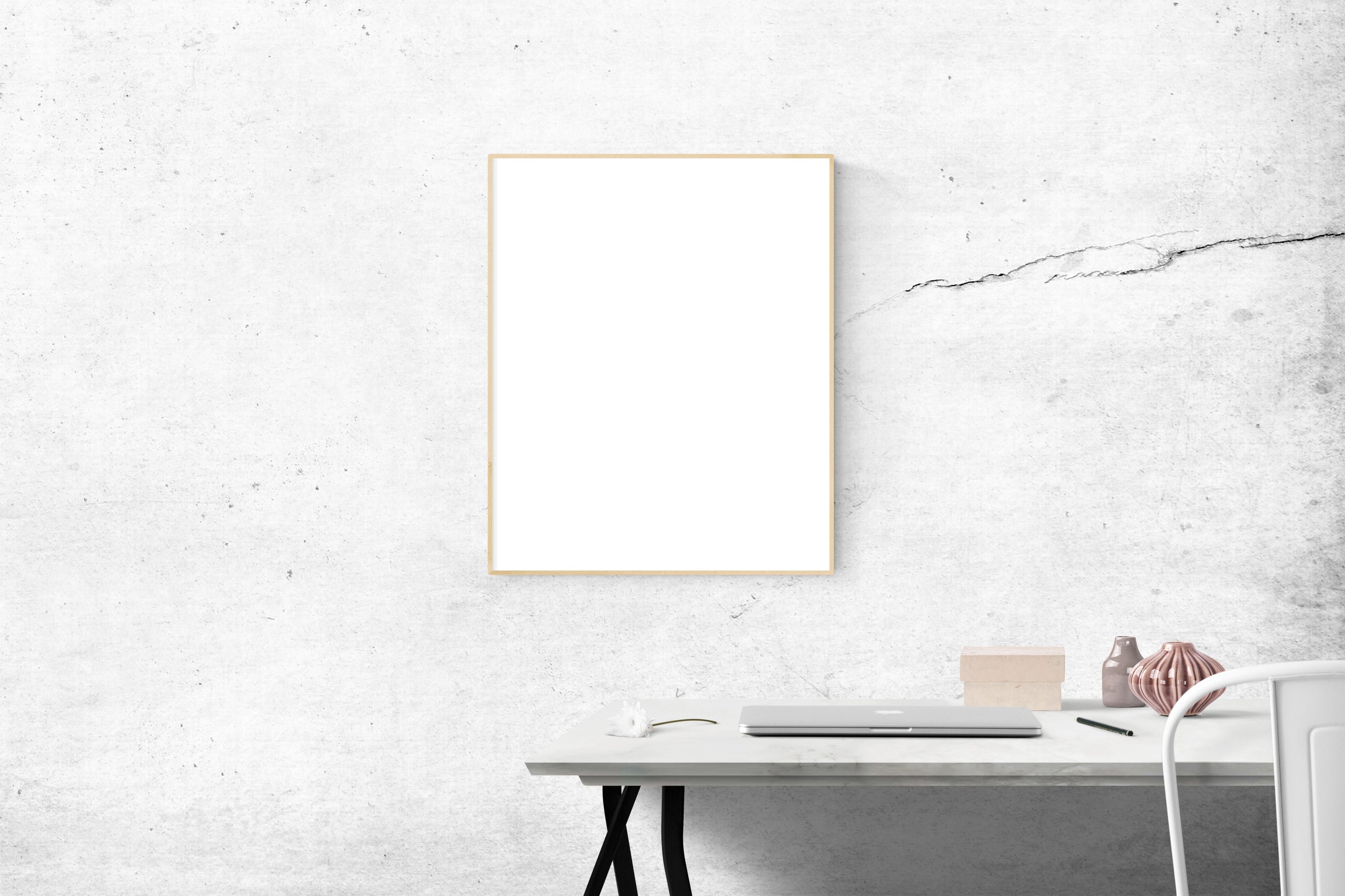 A minimalist workspace with a laptop, blank frame, and textured white wall.