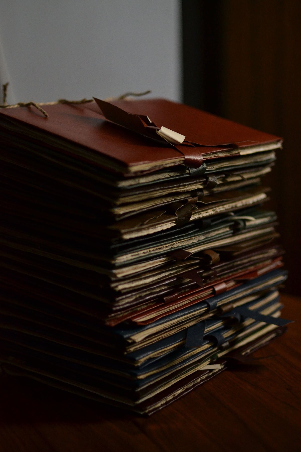 A stack of worn folders and papers on a wooden table in dim light.