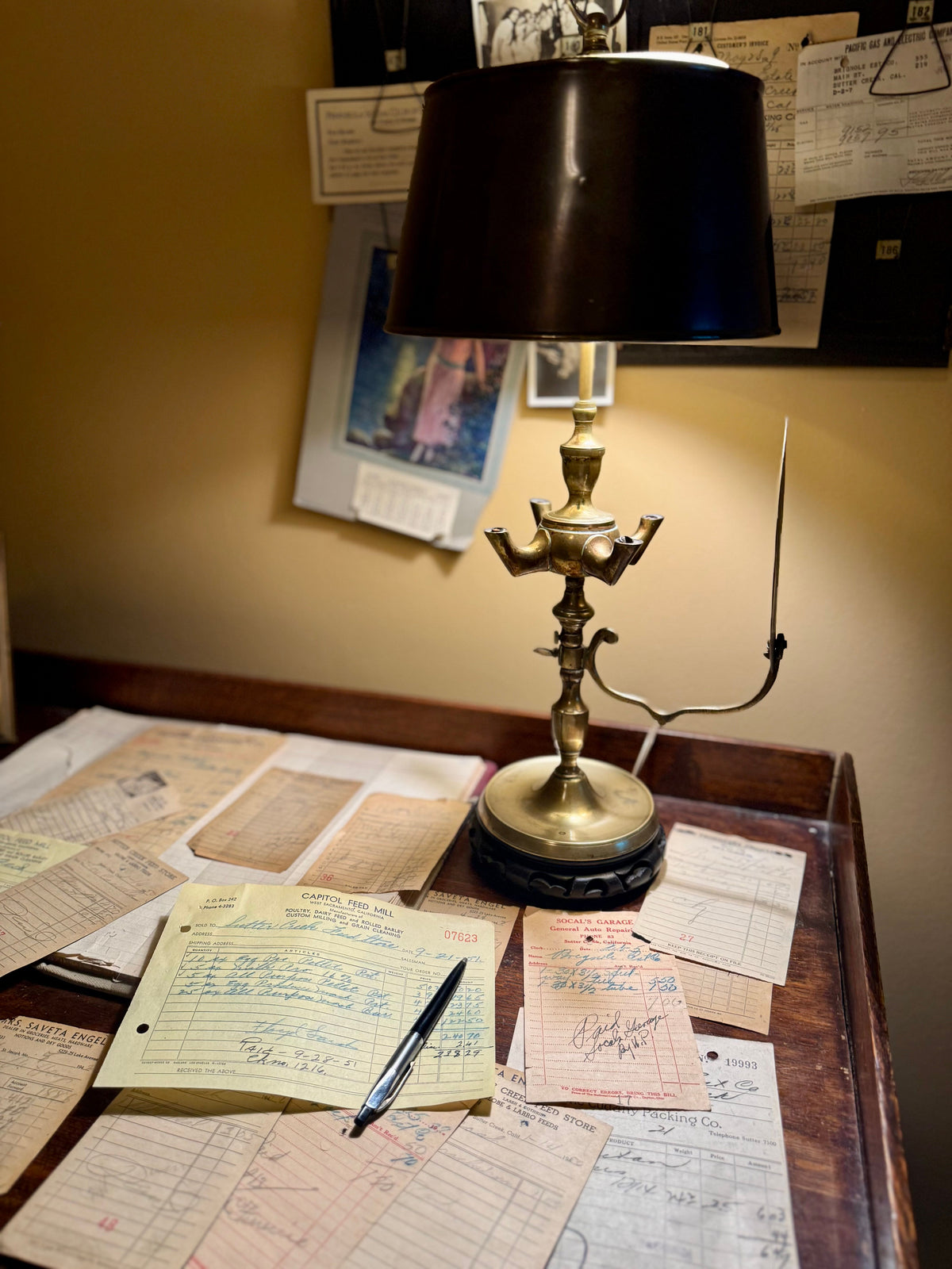 Vintage brass lamp illuminating handwritten invoices and receipts scattered across a wooden desk.
