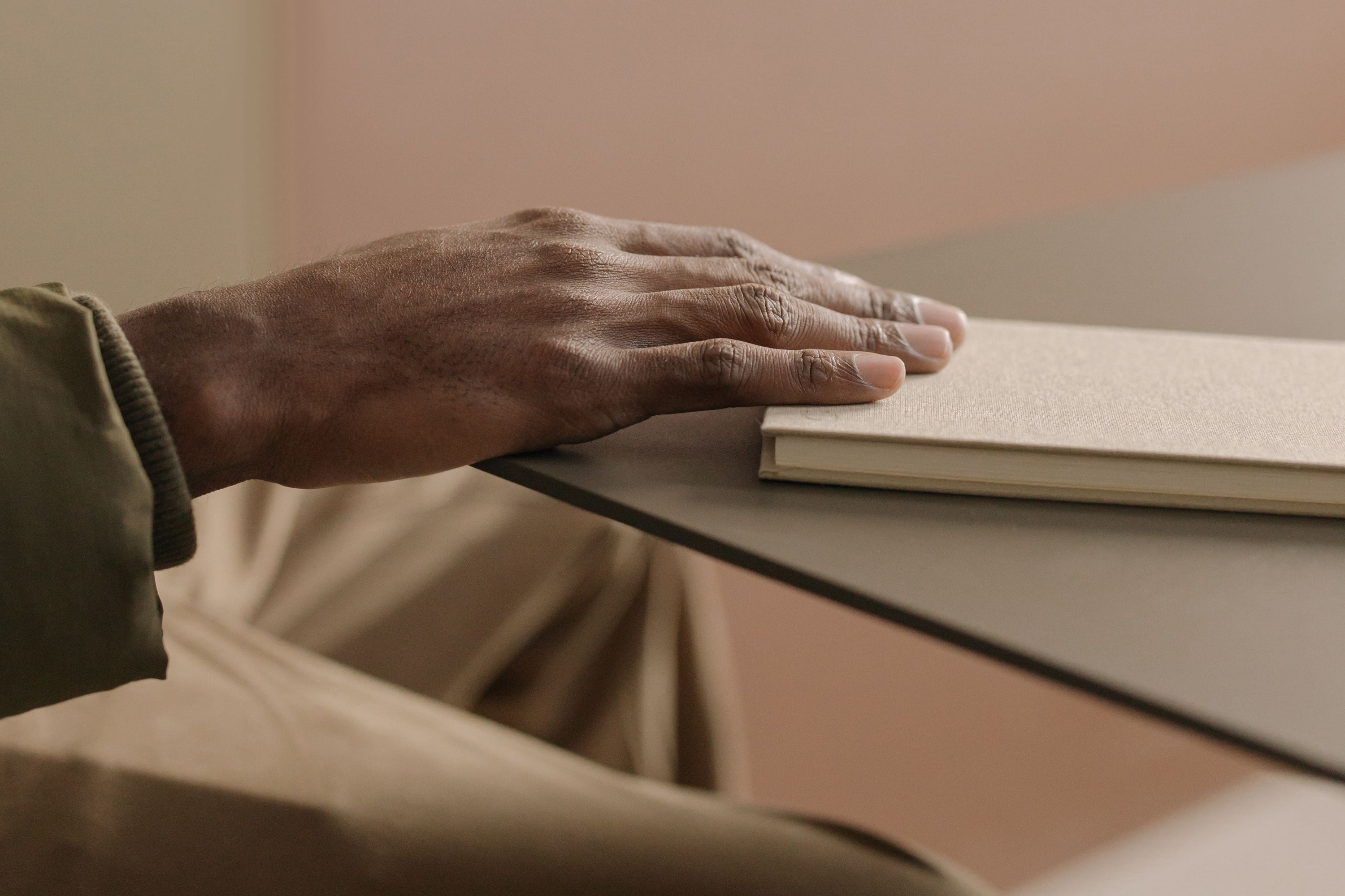 A hand resting on a closed book at a table.
