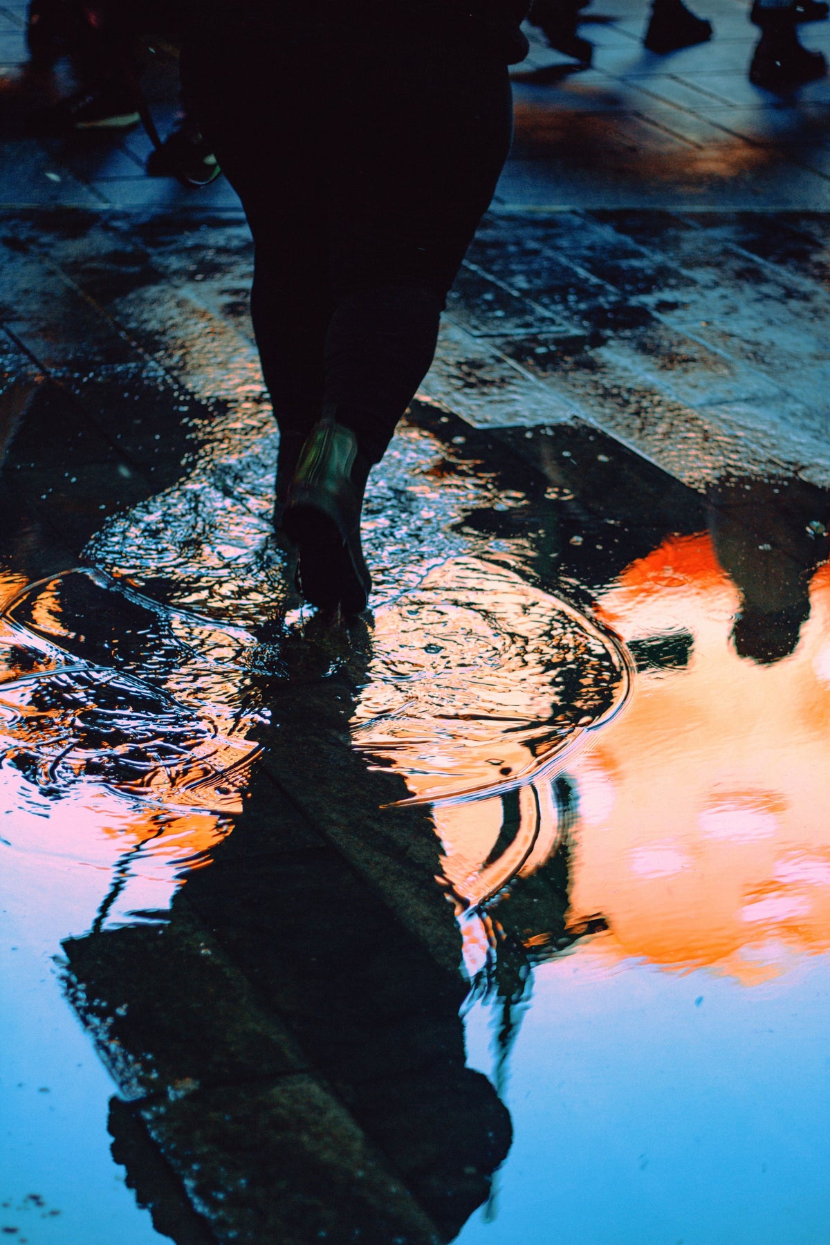 Person walking through a puddle with colorful reflections.