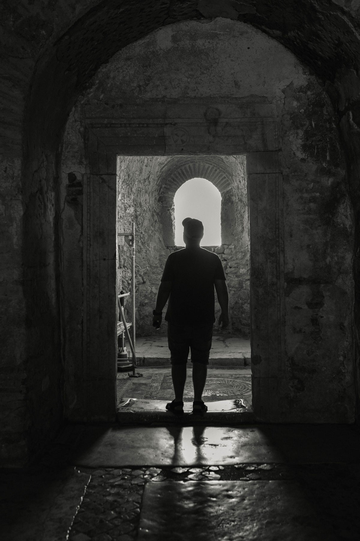 A silhouetted person standing in a stone doorway facing the light.