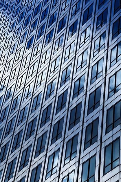 Rows of blue-tinted windows on an office building reflecting the sky and clouds.