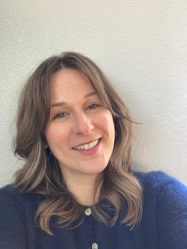 Elizabeth smiling at the camera, with shoulder-length wavy brown hair and a navy sweater.