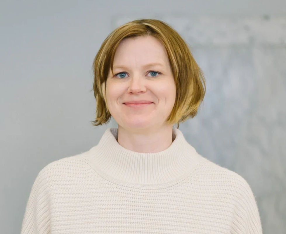 Erika smiling softly, with a short auburn bob and a cream turtleneck sweater.