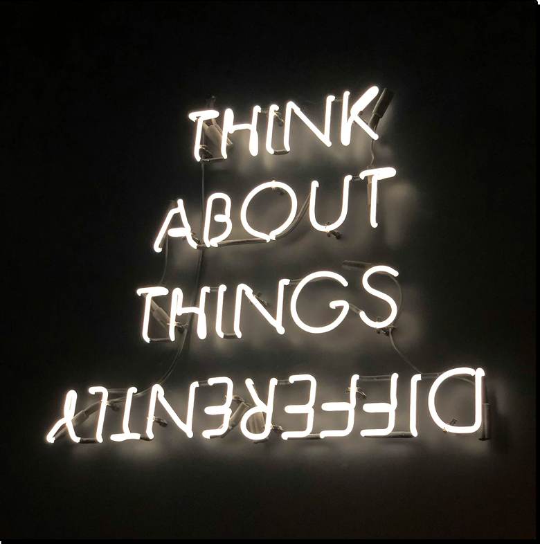 Neon sign on a black wall reading "THINK ABOUT THINGS DIFFERENTLY," with the word "DIFFERENTLY" mounted upside down.