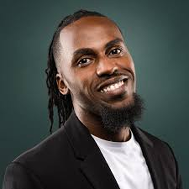 Vincent smiling broadly, with locs and a beard, wearing a black blazer over a white shirt.